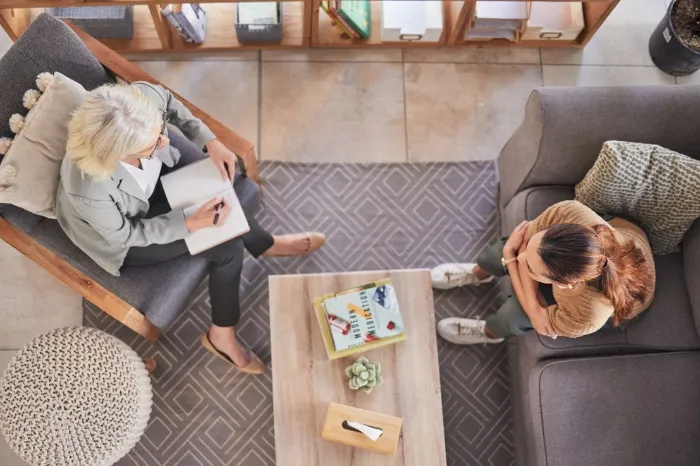 Top view, psychologist and patient woman in consultation office, lounge sofa or talking for anxiety. Senior therapist, depression or mental health for client girl, conversation or discussion above